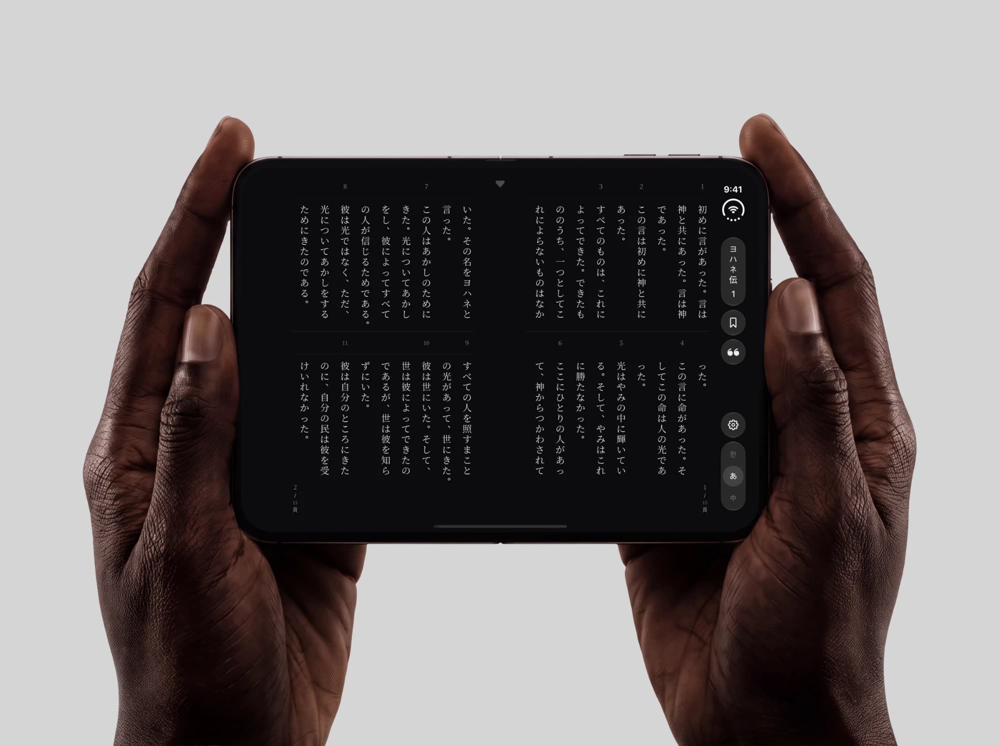 Vertically Verse on iPhone Duo, opened and held in both hands · John 1 in vertical Japanese across a right-bound two-page spread, two tiers a page, verses 1 to 11